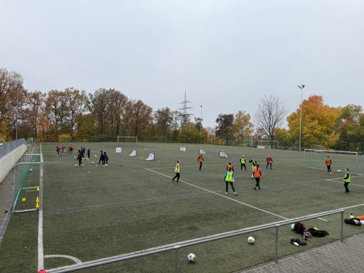 Fußballtraining auf einem Platz mit Spielern in verschiedenen Trikots und Bällen.