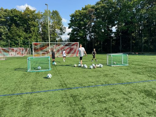 Junge Spieler trainieren auf einem Fußballfeld mit kleinen Toren und Bällen.